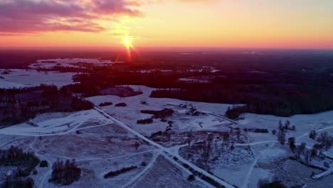 Aerial-drone-view-of-a-snow-covered-landscape-with-the-sun-setting-orange-on-the-horizon