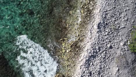 Drone-flying-above-coral-coastline-with-rocks-and-waves-crashing