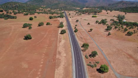 Aerial-View-Of-Car-Driving-Down-A-Long-Dirt-Road-In-Wide-Open-Landscape