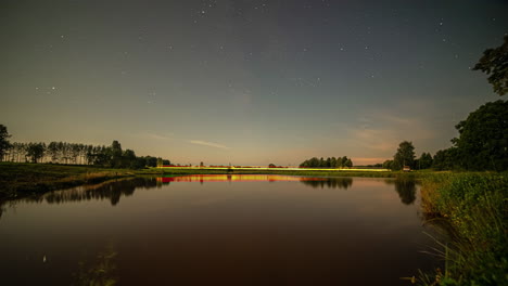 Stars-moving-in-night-sky-over-dam-as-daybreak-arrives,-night-to-day-time-lapse