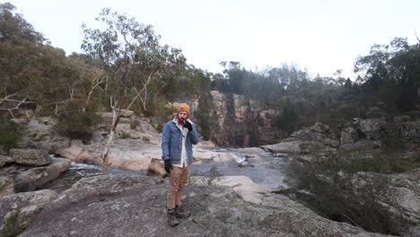 A-bushman-smoking-a-pipe-and-putting-gloves-on-in-the-cold-australian-bush-ontop-of-a-waterfall