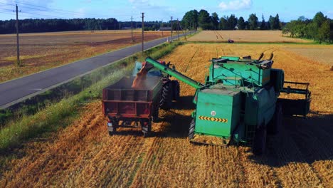 Combine-Harvester-Depositing-Wheat-Into-A-Tractor-Trailer---drone-shot