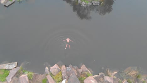 Eine-Vogelperspektive-Luftaufnahme-Eines-Mannes,-Der-Im-Winter-In-Kaltem-Wasser-Auf-Einem-Bauernhofdamm-Schwimmt