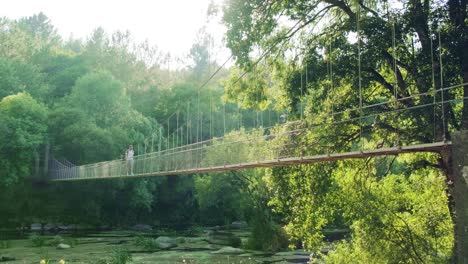 Traveler-walks-along-Sunspension-bridge-in-the-middle-of-dense-foreste,-Outdoors-activities