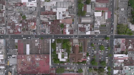Wide-top-down-aerial-footage-of-cars-moving-down-a-road-in-the-outskirts-of-Guatemala-City,-Guatemala