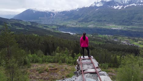 Aerial-moving-backwards-and-revealing-beautiful-woman-standing-on-viewpoint-in-Voss-Norway---Nordheim-slate-mine-looking-towards-Lonavatnet-lake-and-Voss-center