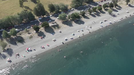 Aerial-shot-in-the-Ranco-lake-in-Chile-of-people-bathing-and-having-fun-in-the-lake-with-cars-parked-near-a-grassfield-with-trees