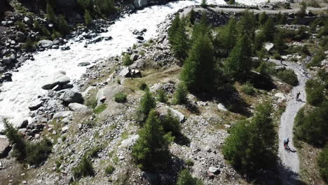 Mountain-stream,-gravel-path-and-fir-forest,-drone-aerial-view-in-the-Swiss-alps