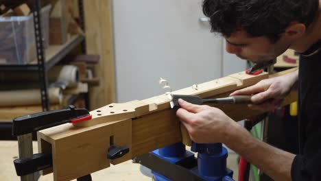 Guitar-maker-working-with-chisel-cutting-out-facets-on-the-back-of-guitar's-neck-at-workshop