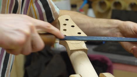Luthier's-hands-filing-back-side-on-guitar's-neck-at-workshop---close-up