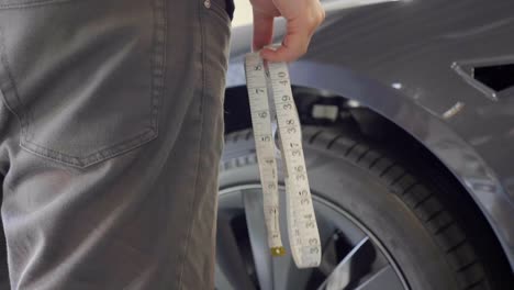 Garage-Workshop-Worker-Holding-Measuring-Tape-near-Car