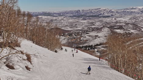 Park-City-Utah-Aerial-v7-adrenaline-rush-extreme-sport-shot,-drone-fly-along-with-skiers-on-mountain-ski-run,-following-by-a-thrilling-downhill-steep-slopes---Shot-with-Mavic-3-Cine---February-2022
