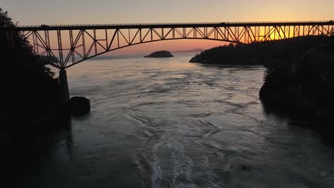Aerial-view-moving-over-a-boat-racing-under-Deception-Pass-Bridge-and-then-passing-over-the-top-of-the-bridge