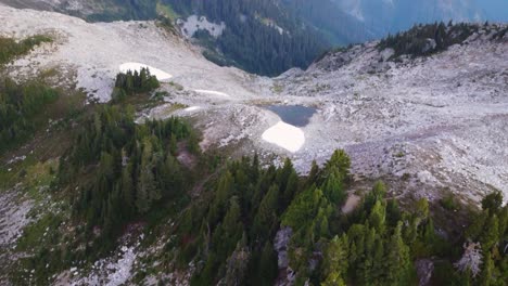 Slow-Tilting-Up-Aerial-Drone-Shot-with-Pine-Trees-and-Small-Lake-with-Rugged-Mountain-Terrain-in-Background-on-Mount-Brew-Canada-BC-4K