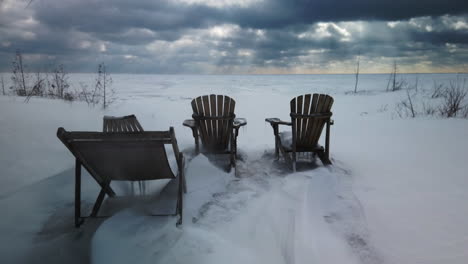 Blasender-Schnee-Wirbelt-Um-Leere-Cottage-Stühle-Herum,-Die-Im-Kanadischen-Winter-An-Einem-Windigen,-Einsamen-See-Sitzen