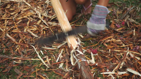 Close-up-of-woman-wearing-gloves-shaving-bark-off-large-stick-with-machete
