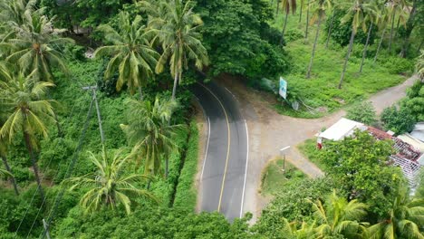White-car-and-motorbike-drive-around-a-bend-in-the-tropical-jungle-of-Lombok-Island,-aerial