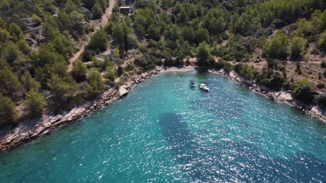 Aerial-fly-away-shot-of-secluded-private-beach-with-anchored-boats-over-the-beautiful-turqoise-waters-of-Adriatic-Sea-in-Brac,-Croatia