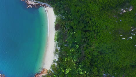 Drone-shot-traveling-to-the-right-above-a-little-tropical-bay-with-a-beach-and-a-hill-full-of-tropical-vegetation-during-the-day