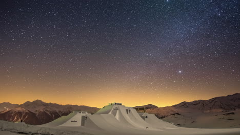 Orbiting-stars-time-lapse-in-brilliant-night-sky-over-snowpark-with-impressive-ski-jumps,-multiple-shooting-stars