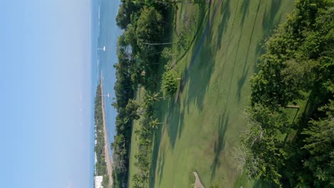 Vertical-Shot-Of-Playa-Dorada-Golf-Course-With-Sailboats-On-The-Beach-In-Puerto-Plata,-Dominican-Republic