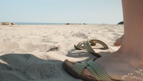 Female-putting-on-sandals-on-sandy-beach