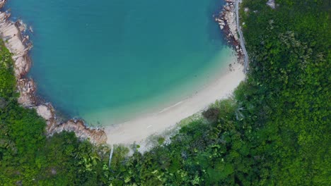 Drone-shot-rotating-above-a-little-tropical-bay-with-a-beach-and-a-hill-full-of-tropical-vegetation-during-the-day