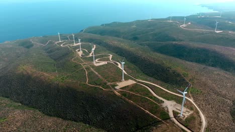 Aerial-tracking-view-of-a-windmills-line-on-rugged-mountain-by-the-Ocean