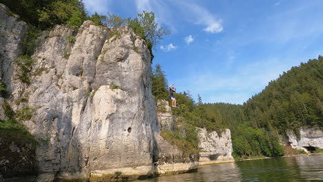 A-young-jumps-from-a-high-rocky-cliff-into-the-water-of-the-Doubs-river,-Switzerland