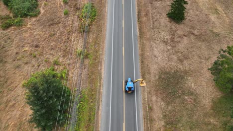 Drone-shot-of-a-tractor-driving-down-the-highway-while-mowing-the-sloped-ditch-in-rural-America