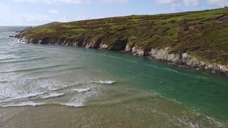 Aerial-shot-Cornwall-seaside-patchwork-green-and-gentle-waves-pan-to-horizon