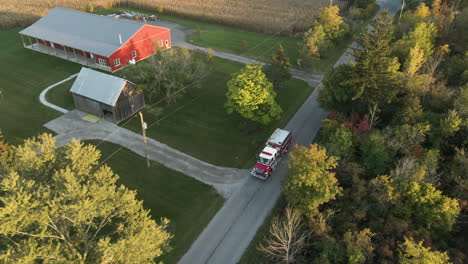 Aerial-Tracking-View-of-Emergency-Fire-Truck-Vehicle-Driving-Moving-along-Countryside-Road-at-Rural-Neighborhood,-Rescue-First-Responder-Alert-Mission,-Local-Homes-and-Landscape-Around
