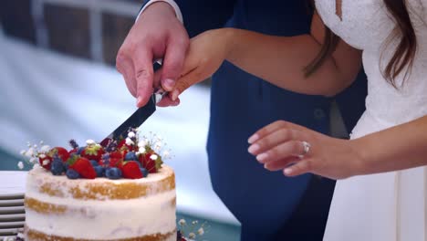 Hands-of-newlywed-couple-cutting-fruit-wedding-cake-together,-close-up
