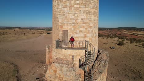 Middle-aged-man-wearing-a-red-shirt,-camouflage-shorts-and-a-cap-fly-back-shoot-in-a-islamic-watch-tower-in-Soria,-Spain