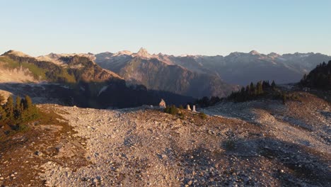 Sonnenuntergang-Luftdrohnenaufnahme-Nähert-Sich-Einer-Einsamen-Hütte-Auf-Dem-Mount-Brew-Peak-Mit-Felsiger-Berglandschaft-Im-Hintergrund-In-Kanada-Bc-4k