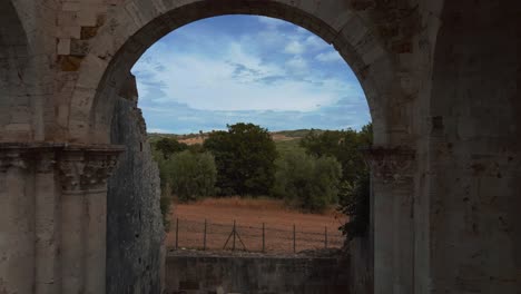 Flying-through-Abbazia-di-San-Bruzio,-an-old-damaged-ruin-of-an-abandoned-medieval-monastery-abbey-church-in-Tuscany-of-the-11th-century-surrounded-by-olive-trees-in-Italy