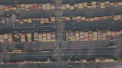 Top-down-aerial-footage-of-a-shipping-yard-full-of-colorful-shipping-containers-with-trucks-driving-in-between-them