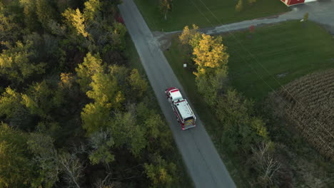 Aerial-Tracking-View-of-Emergency-Fire-Truck-Vehicle-Driving-Fast-along-Countryside-Road-with-Flashing-Lights,-Rescue-First-Responder-Mission-for-Fire-Fighting-Accident-Alert,-Route-Through-Landscape