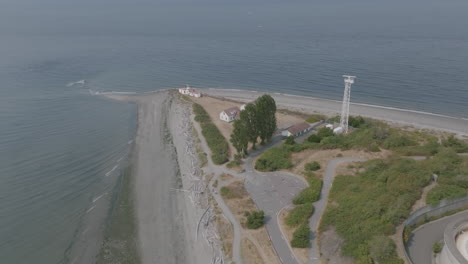 Wide-aerial-footage-showing-the-water-treatment-plant,-radar-station-and-West-Point-Lighthouse-at-the-tip-of-a-landmass-in-Seattle,-WA
