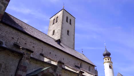 Wide-tracking-shot-revealing-the-exterior-and-bell-tower-of-the-romanesque-Collegiate-church-of-San-Candido,-Italy