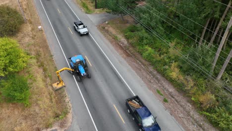 Drone-shot-of-tractor-with-a-flail-mower-attachment-as-it-slowly-drives-down-the-highway-to-cut-down-on-weeds