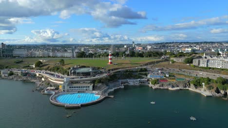 A-drone-video-flying-into-Plymouth-Hoe,-showing-Smeaton's-Tower-Lighthouse-and-the-Plymouth-Lido-swimming-pool