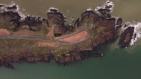 Aerial-top-down-shot-of-cars-on-viewpoint-of-rocky-hill-surrounded-by-ocean-in-Punta-Ballena,Uruguay