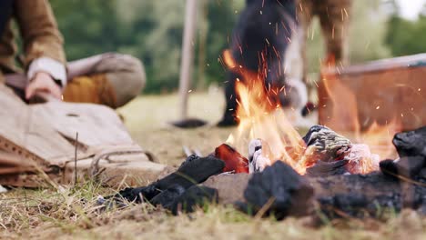 Static-close-up-of-a-person-dressed-in-medieval-costume-applying-bellows-to-campfire-in-slow-motion