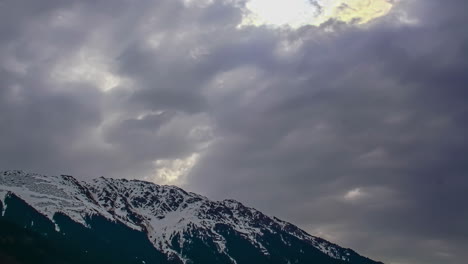 Tiro-De-ángulo-Bajo-De-Nubes-Oscuras-Que-Se-Mueven-Sobre-El-Pico-De-La-Montaña-Cubierta-De-Nieve-En-Timelapse