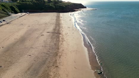 Pull-Back-Drone-shot-of-waves-hitting-the-sand-of-Empty-Exmouth-Beach,-Devon