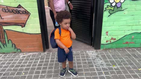 Adorable-and-shy-two-year-old-african-european-child-a-little-upset-after-his-first-nursary-day-after-summer-vacations-followed-by-mum