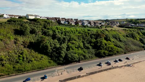 Parallax-drone-shot-of-Marine-Drive-promenade-at-Exmouth-Beach,-Devon-revealing-Foxholes-Hill-residential-area-on-top-of-hill-on-clear-sunny-morning
