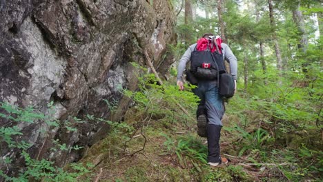 Hiker-Walking-Away-From-Camera-Beside-Rock-Wall---Mackenzie-Range,-Vancouver-Island,-BC,-Canada