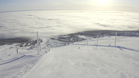Aerial-flying-behind-a-skier-above-a-ski-slope-with-a-view-of-sun-shining-over-the-clouds